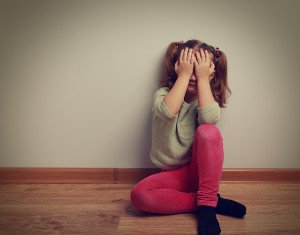 Frightened crying kid girl sitting on the floor with closed face the hands. Vintage closeup portrait